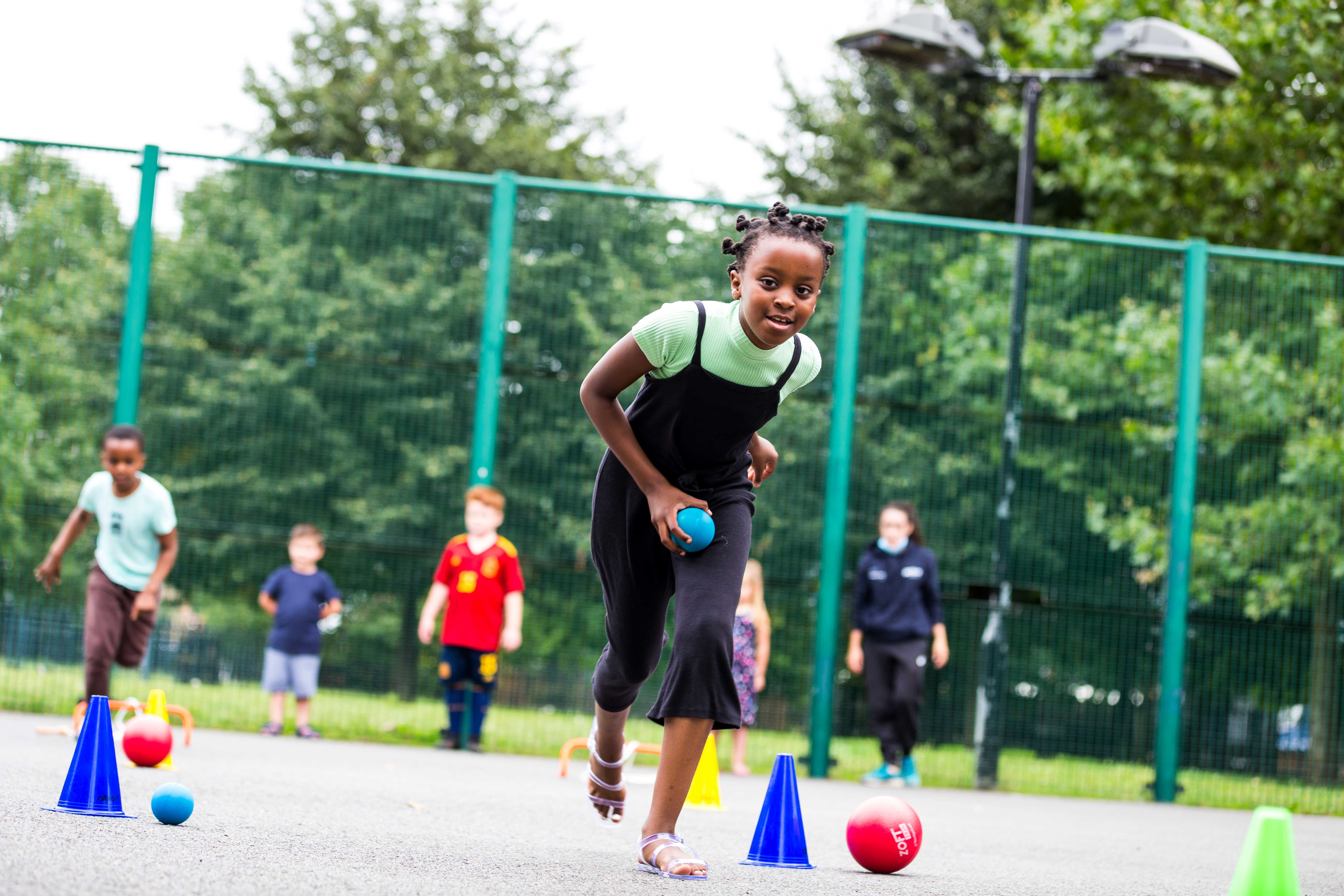 Children in a playground playing with colourfuls balls and cones